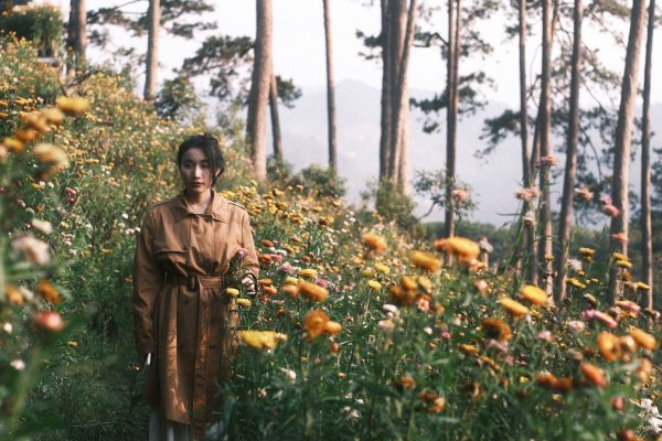 Woman in trench coat among colorful flowers for smart outdoor layering fashion